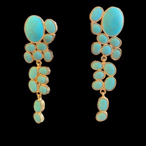 May include: A pair of long, dangling earrings with turquoise stones set in gold. The stones are various shapes and sizes, and they are arranged in a cascading pattern.