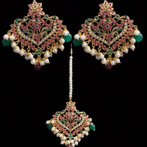 Pode incluir: Um conjunto de joias douradas com brincos e uma peça de cabeça. Os brincos e a peça de cabeça apresentam um design floral com detalhes vermelhos, verdes e brancos. O conjunto inclui pérolas brancas penduradas e pedras preciosas verdes e vermelhas.