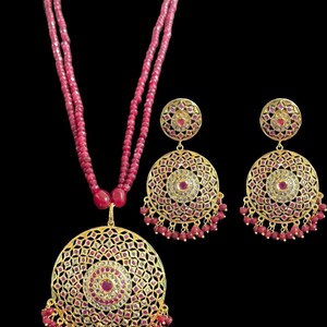 May include: A gold necklace and earrings set with a red beaded chain and a large round pendant with intricate detailing and red and white gemstones.
