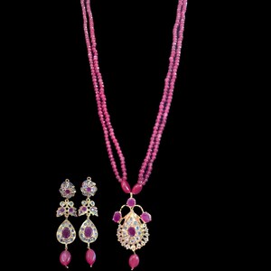 Peut inclure: Un collier de pierres précieuses en rubis rose avec une paire de boucles d'oreilles assorties. Le collier a un pendentif à motif floral et est en or. Les boucles d'oreilles sont également en or et ont une forme de larme.