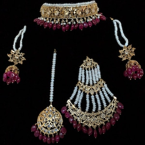 Peut inclure: Un ensemble de bijoux de mariée indien traditionnel comprenant un collier en or avec des pierres rouges et blanches, des boucles d'oreilles assorties, une coiffe et un tikka.