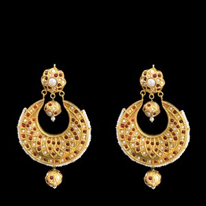 May include: A pair of gold earrings with red and white stones. The earrings are shaped like a crescent moon and have a dangling pearl.