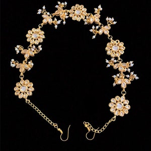 May include: Gold chain with a series of pearl and flower-shaped charms. The chain has two hooks at the ends.