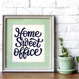 Könnte beinhalten: Ein gerahmter Druck mit weißem Hintergrund und schwarzem Text, der "Home Sweet Office" lautet. Der Rahmen ist silberfarben mit einer hellgrünen Passepartout. Der Druck steht auf einem Holztisch mit einer grünen Topfpflanze und einem kleinen Kaktus in einem grauen Topf.