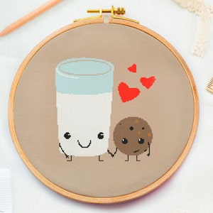 May include: Embroidered hoop art featuring a cartoon glass of milk and a chocolate chip cookie, both with smiling faces and arms and legs. The glass of milk is holding a red heart in its hand and there are three red hearts floating above the characters.