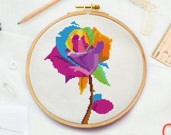 May include: A colorful rainbow rose cross-stitch embroidery project in a wooden embroidery hoop. The rose is made with pink, purple, blue, green, yellow, and orange thread.