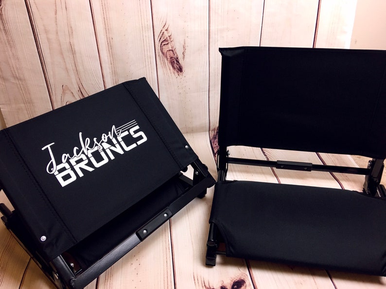 Puede incluir: Dos sillas plegables negras con un dise&ntilde;o blanco. La silla de la izquierda tiene el texto "Jackson Bruins" impreso en el respaldo.