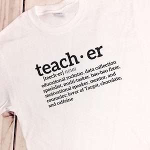 Op de afbeelding: Wit T-shirt met zwarte tekst die "teacher [teech-er] noun educational rockstar, data collection specialist, multi-tasker, boo-boo fixer, motivational speaker, mentor, and counsellor; lover of Target, chocolate, and caffeine" luidt.