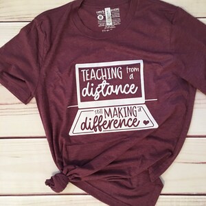May include: Burgundy t-shirt with white text that reads "Teaching from a distance still making a difference" with a small heart icon.