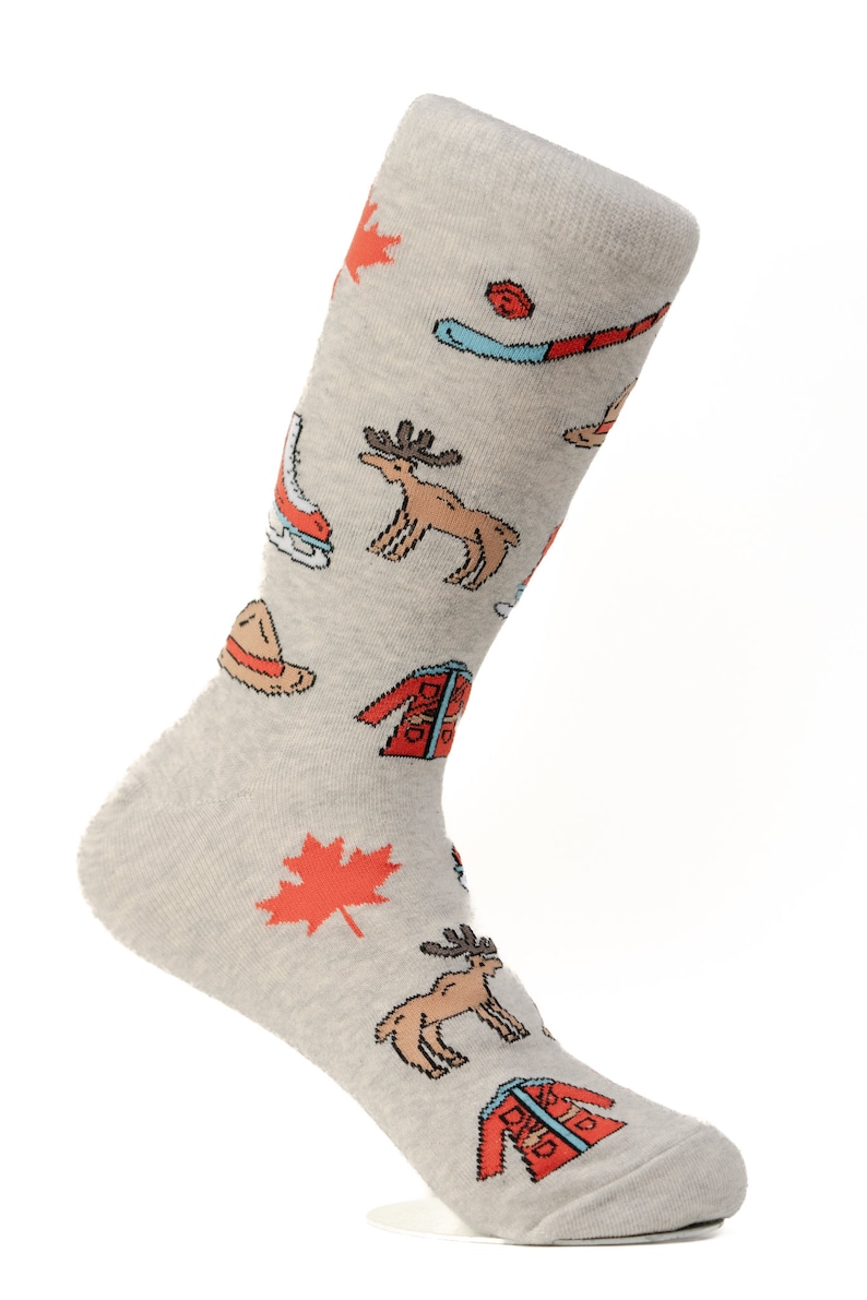 May include: A pair of gray socks with a Canadian theme. The socks feature images of a moose, a maple leaf, a hockey stick, a toque, and a winter jacket.