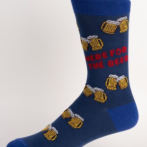 May include: Navy blue socks with a pattern of yellow beer mugs and the red text "HERE FOR THE BEER." The socks have blue heels, toes, and cuffs. These socks are a fun accessory for beer lovers.