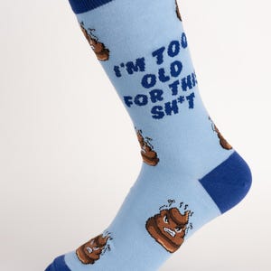 May include: Light blue socks with the text "I'M TOO OLD FOR THIS SH*T" and cartoon poop graphics. The socks have dark blue cuffs, heels, and toes. The socks are made of a soft, comfortable material.