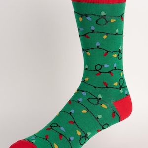 May include: Green Christmas-themed sock with a red cuff, heel, and toe. The sock is decorated with a pattern of colorful Christmas lights in red, blue, and yellow. The lights are strung together with black lines.