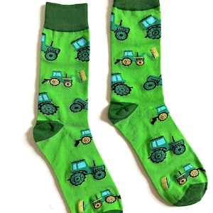 May include: A pair of green socks with a repeating pattern of blue and yellow tractors. The socks have a green cuff, heel, and toe. The tractors have blue cabs and yellow wheels.