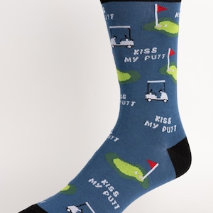 May include: Blue golf socks with a black heel and toe, featuring golf carts, green putting greens, and red flags. The phrase "Kiss My Putt" is printed on the socks.