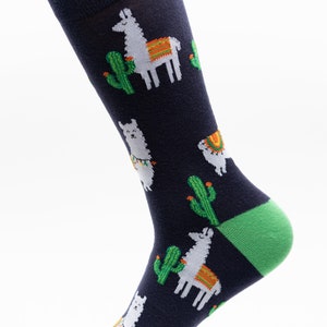 May include: A pair of dark blue socks with a green heel and toe. The socks feature a white llama and green cactus pattern.