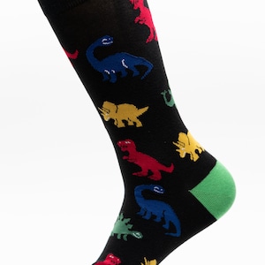 以下が含まれることがあります： 赤、青、黄色のカラフルな恐竜模様の黒い靴下。 靴下のかかととつま先は緑色です。 楽しくて遊び心のあるアクセサリーです。