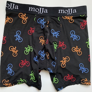 Puede incluir: Bóxers negros con un patrón repetido de bicicletas de colores. La cintura es negra con la palabra "MOJJA" impresa en blanco.