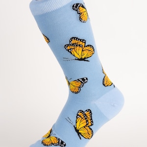 May include: Light blue socks with a repeating pattern of orange and black monarch butterflies. The socks are knee-high and made of a soft material. The butterflies have detailed wing patterns.