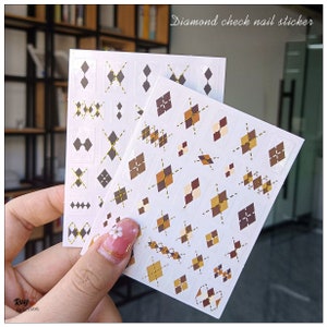 May include: Two sheets of nail stickers with a diamond check pattern in brown, beige, and gold. The text "Diamond check nail sticker" is printed at the top of the image.