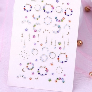 May include: A sheet of nail art stickers with a variety of designs, including stars, moons, rings, and other geometric shapes. The stickers are on a white background and are arranged in rows. The text "A025" is printed on the sheet.