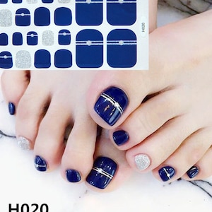 May include: Blue and silver toe nail polish stickers with a silver rhinestone design. The stickers are shown on a person's toes. H020