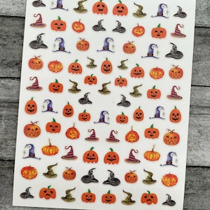 May include: A sheet of Halloween-themed stickers featuring orange jack-o'-lanterns with carved faces, witch hats in black, purple, and green, and striped witch hats. The stickers are arranged in a grid pattern on a white background.
