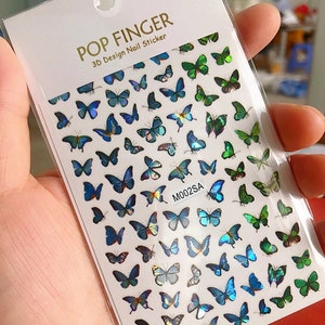 May include: A sheet of nail stickers with a design of iridescent blue and green butterflies. The sheet is labeled "POP FINGER 3D Design Nail Sticker" and "M002SA".