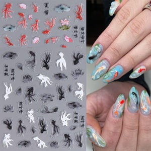 May include: Nail art stickers featuring koi fish, lotus flowers, and Chinese characters in red, black, and white. The stickers are on a gray background. The image also shows a hand with painted nails featuring koi fish and water designs.