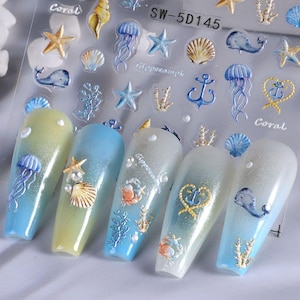 May include: Nail art stickers featuring an ocean theme. The stickers include images of starfish, seashells, jellyfish, whales, and anchors. The nails are painted with a gradient of blue, yellow, and white, and decorated with 3D embellishments.