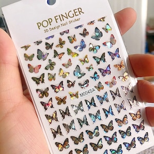 May include: A sheet of iridescent butterfly nail stickers. The stickers are arranged in rows and feature a variety of butterfly designs, including butterflies with wings that are striped, spotted, and solid colors. The sheet is labeled "POP FINGER 3D Design Nail Sticker" and "M004SA".
