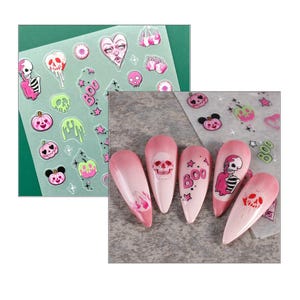 Może przedstawiać: Różowe i białe naklejki na paznokcie z motywami Halloween, w tym czaszki, dynie i napis "BOO!"