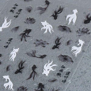 May include: Clear sticker sheet featuring black and white koi fish and lotus flower designs. The stickers have a watercolor effect and include Chinese characters. The koi fish are in various poses, and the lotus flowers are in different stages of bloom.