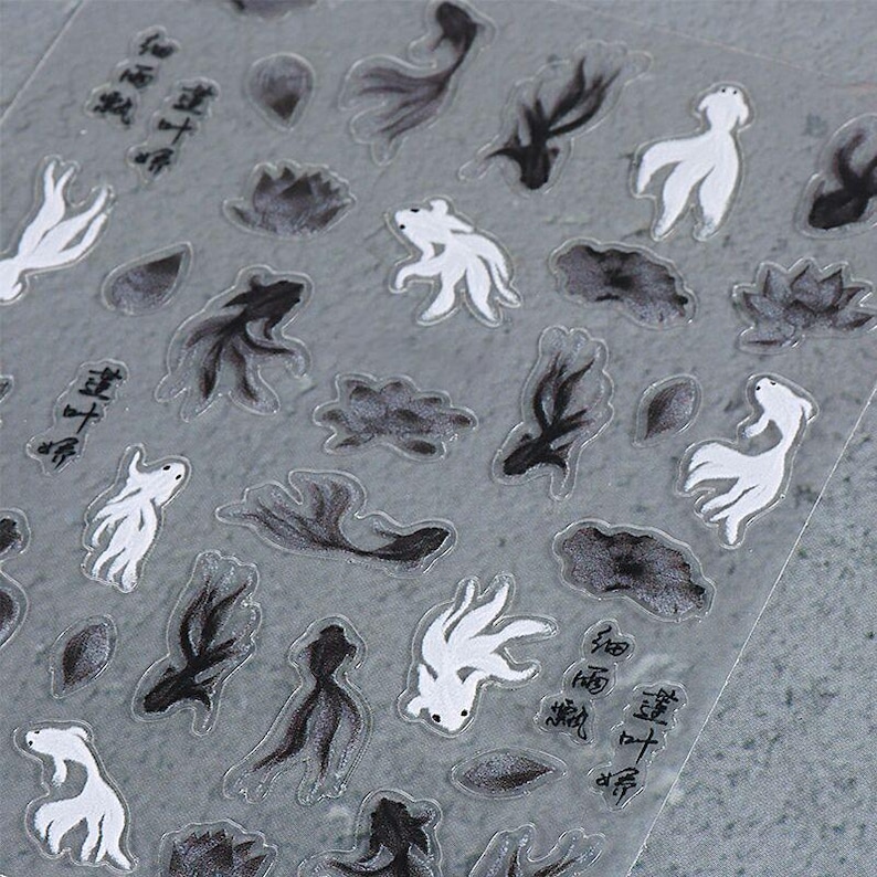 May include: Clear sticker sheet featuring black and white koi fish and lotus flower designs. The stickers have a watercolor effect and include Chinese characters. The koi fish are in various poses, and the lotus flowers are in different stages of bloom.