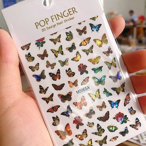 May include: A sheet of nail stickers with a variety of colorful butterfly designs. The stickers are 3D and have a holographic finish. The sheet is labeled "POP FINGER 3D Design Nail Sticker" and "M006SA".