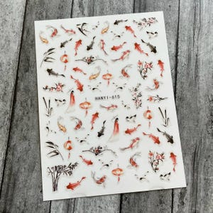 May include: A sheet of clear nail stickers with a variety of designs, including red and black koi fish, cherry blossoms, bamboo, and lanterns. The text "HANYI-615" is printed on the sheet.