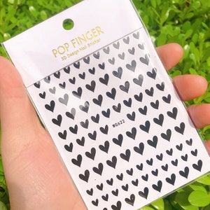 Op de afbeelding: Een vel met zwarte hartvormige nagelstickers met de tekst "POP FINGER 3D Design Nail Sticker WG622".