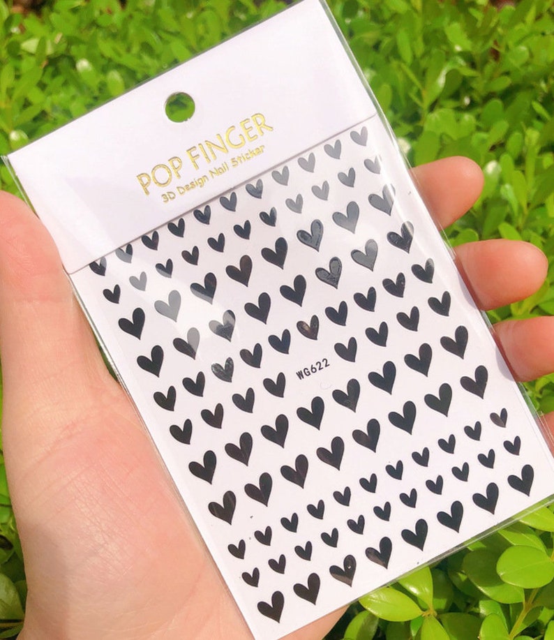 Op de afbeelding: Een vel met zwarte hartvormige nagelstickers met de tekst "POP FINGER 3D Design Nail Sticker WG622".