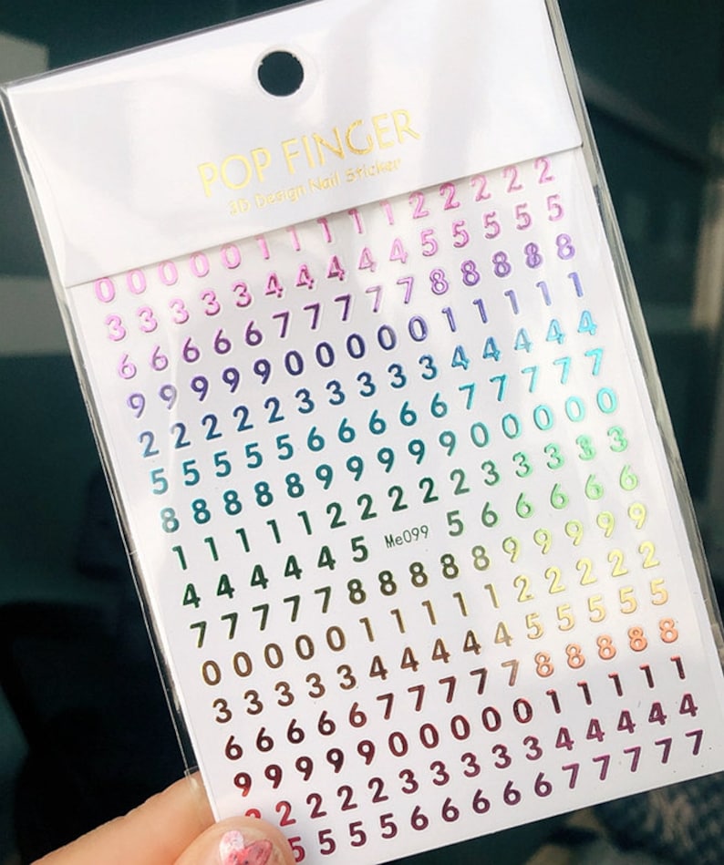 May include: A sheet of rainbow holographic nail stickers with numbers 0-9. The stickers are arranged in rows and columns, with each number appearing multiple times. The stickers are packaged in a clear plastic bag with the brand name "POP FINGER" and the text "25 Design Nail Stickers" printed on the front.