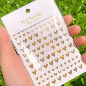 Op de afbeelding: Een vel met gouden hartvormige nagelstickers met een holografische afwerking. Het vel is gelabeld met "POP FINGER 3D Design Nail Sticker" en "WG422".