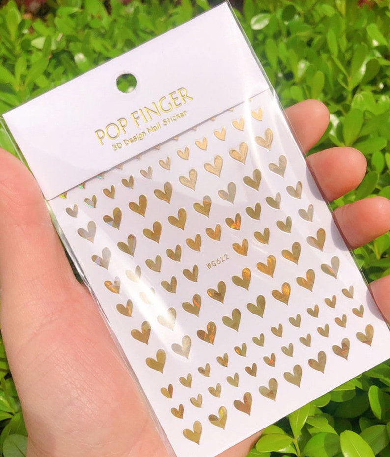 Op de afbeelding: Een vel met gouden hartvormige nagelstickers met een holografische afwerking. Het vel is gelabeld met "POP FINGER 3D Design Nail Sticker" en "WG422".