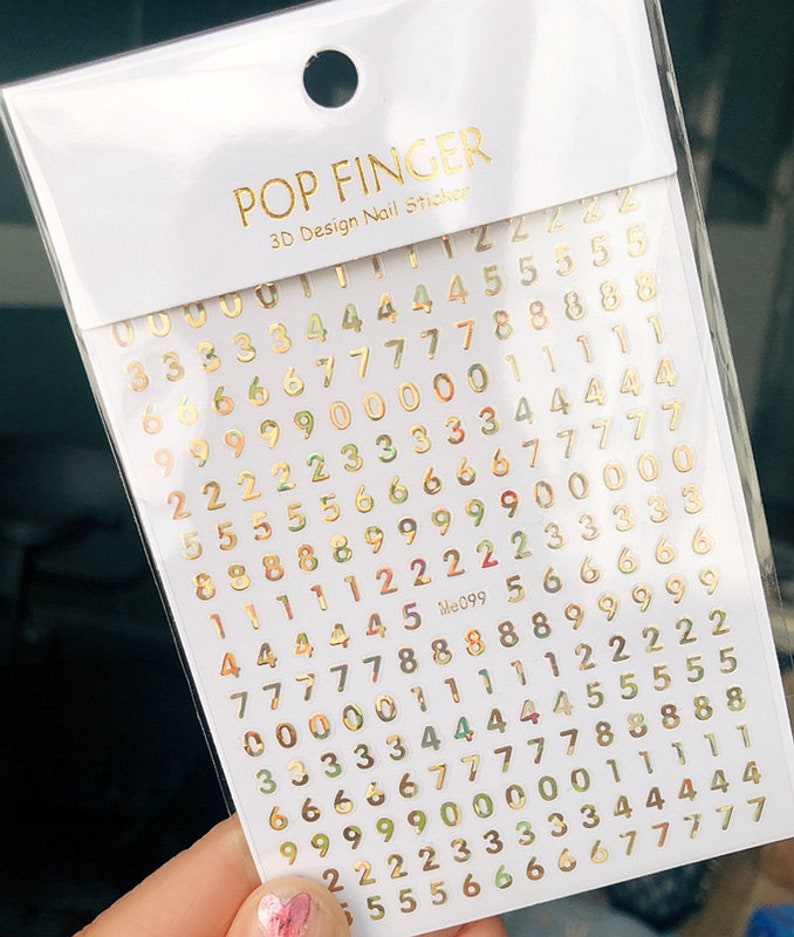 May include: Gold number nail stickers on a white background. The numbers range from 0 to 9 and are arranged in a grid pattern. The stickers are designed for nail art and are labeled "POP FINGER 3D Design Nail Sticker".