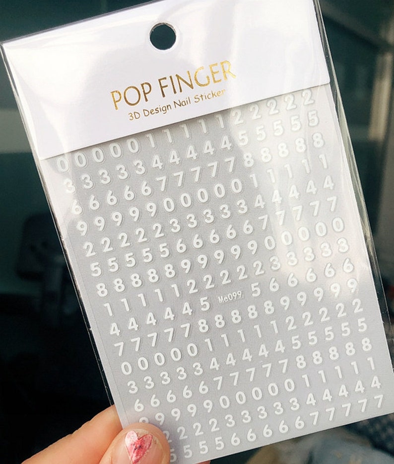 May include: A sheet of white nail stickers with numbers 0-9 printed on them. The stickers are arranged in rows and columns. The sheet is labeled "POP FINGER 3D Design Nail Sticker" and "Me099".