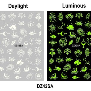 Pu&ograve; includere: Due fogli di adesivi per unghie con una variet&agrave; di disegni celesti, tra cui lune, stelle, cristalli e occhi. Il foglio a sinistra &egrave; bianco su sfondo grigio, e il foglio a destra &egrave; verde su sfondo nero. Il testo "DZ42SA" appare su entrambi i fogli.