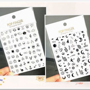 May include: Two sheets of black and white nail stickers with 30 different designs. The designs include crowns, stars, moons, hearts, snakes, crosses, infinity symbols, and more.