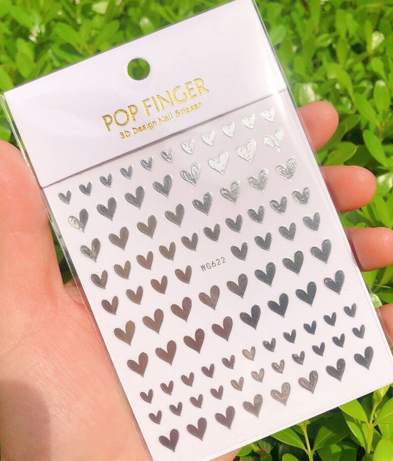 Op de afbeelding: Een vel zilveren nagelstickers met een ontwerp van kleine hartjes. Het vel is gelabeld met "POP FINGER 3D Design Nail Sticker" en "WG622".