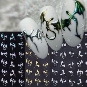 May include: Nail art stickers featuring dragon designs in silver, gold, and iridescent finishes. The stickers are displayed on a black background, with several dragon designs on white nail polish.