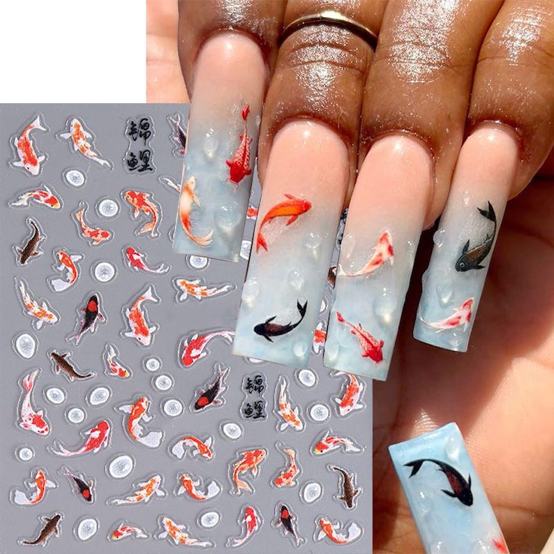 May include: Nail art featuring koi fish designs in red, orange, black, and white. The nails have a gradient blue and white background, with some nails featuring 3D water droplet accents. A sheet of koi fish nail decals is also visible.