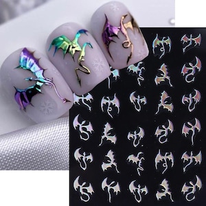 May include: Nail art featuring iridescent dragon decals. Three nails showcase dragon designs with a holographic effect, while a sheet of additional decals is visible. The dragons have detailed wings and tails, with a color shift from green to purple.