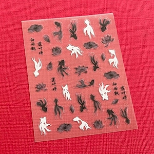 May include: Clear sticker sheet with a repeating pattern of black and white koi fish, lily pads, and Chinese characters. The sticker sheet is on a red background.